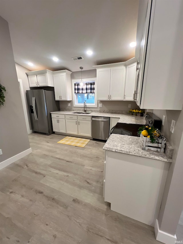 kitchen featuring light hardwood / wood-style flooring, pendant lighting, white cabinetry, appliances with stainless steel finishes, and light stone counters