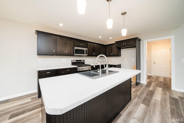 kitchen with sink, light wood-type flooring, hanging light fixtures, stainless steel appliances, and a center island with sink