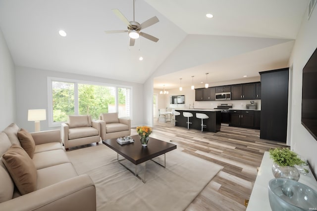 living room with ceiling fan with notable chandelier, light wood-type flooring, and high vaulted ceiling