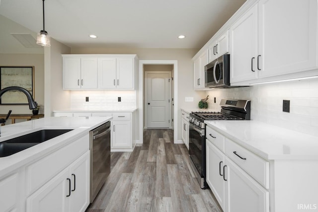 kitchen with appliances with stainless steel finishes, white cabinetry, light hardwood / wood-style flooring, pendant lighting, and sink