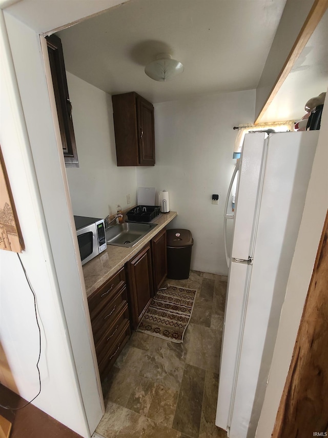 kitchen with dark brown cabinetry, sink, and white refrigerator