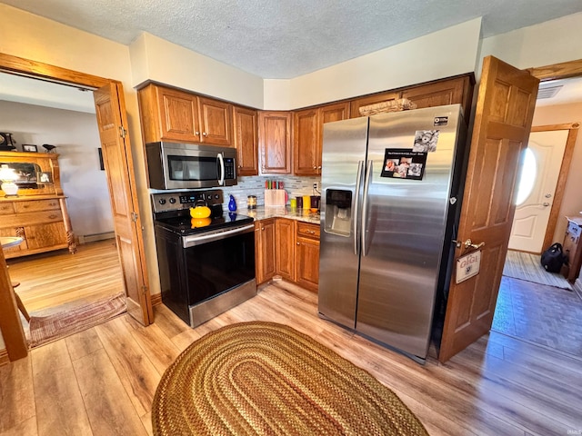 kitchen with decorative backsplash, stainless steel appliances, light wood-type flooring, a baseboard radiator, and a textured ceiling