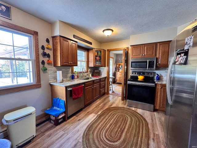 kitchen with appliances with stainless steel finishes, sink, light wood-type flooring, light stone counters, and decorative backsplash