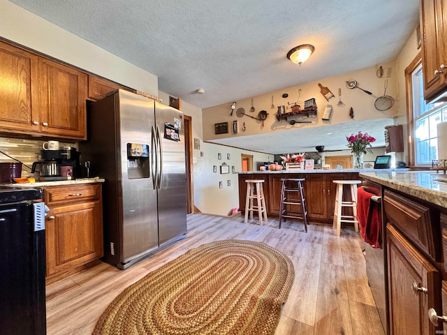 kitchen with stainless steel refrigerator with ice dispenser, black range, a textured ceiling, light hardwood / wood-style floors, and tasteful backsplash