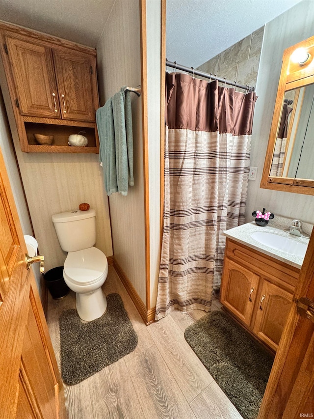 bathroom with a textured ceiling, toilet, walk in shower, vanity, and hardwood / wood-style flooring