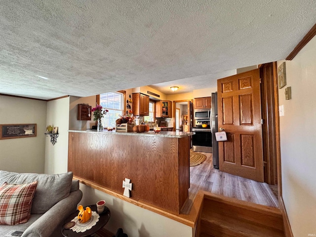 kitchen featuring appliances with stainless steel finishes, kitchen peninsula, a textured ceiling, and light wood-type flooring