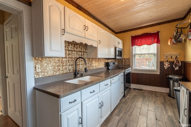 kitchen with dark hardwood / wood-style floors, wooden walls, sink, white cabinetry, and appliances with stainless steel finishes