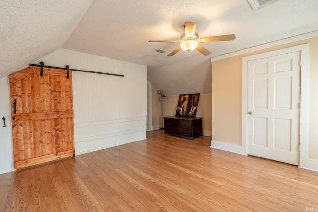 bonus room featuring light hardwood / wood-style flooring, a textured ceiling, a barn door, and lofted ceiling