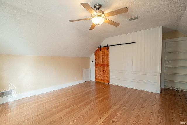 bonus room with wood-type flooring, a barn door, a textured ceiling, ceiling fan, and lofted ceiling