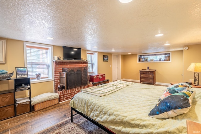 bedroom featuring a textured ceiling, a brick fireplace, and hardwood / wood-style floors