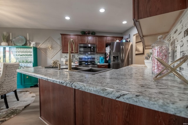 kitchen featuring decorative backsplash, appliances with stainless steel finishes, light stone countertops, light wood-type flooring, and sink