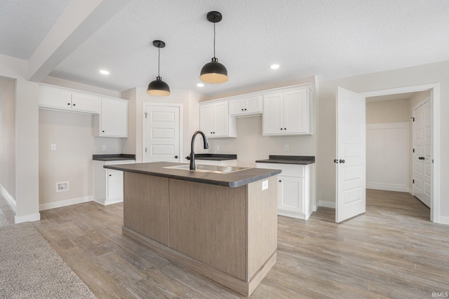 kitchen featuring white cabinetry, decorative light fixtures, an island with sink, light hardwood / wood-style floors, and sink