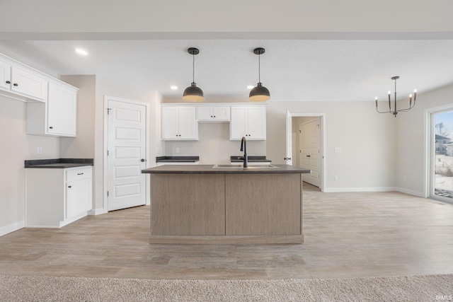 kitchen featuring white cabinetry, a kitchen island with sink, decorative light fixtures, and sink