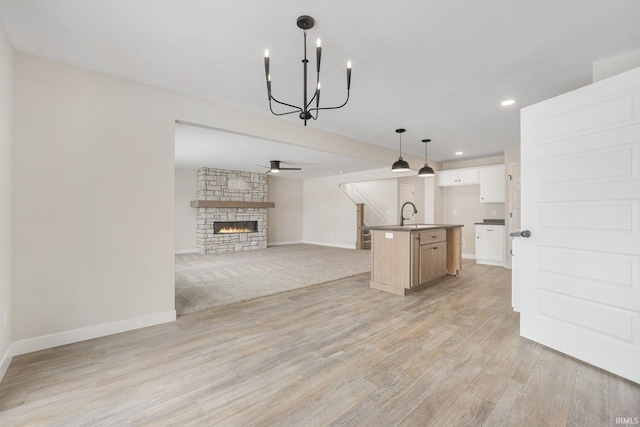 unfurnished living room featuring sink, light wood-type flooring, a fireplace, and ceiling fan with notable chandelier