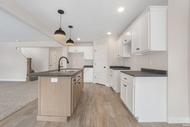 kitchen featuring a center island with sink, decorative light fixtures, white cabinets, a textured ceiling, and sink