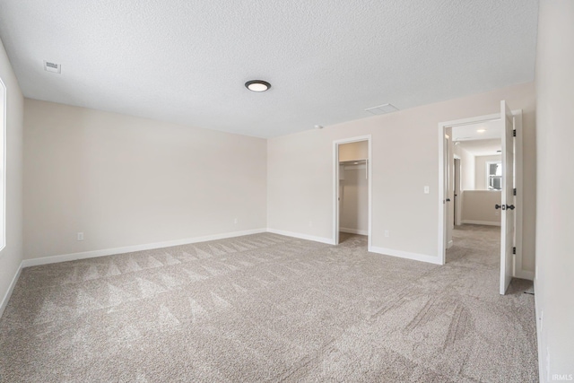 unfurnished bedroom with a textured ceiling, a closet, a walk in closet, and light carpet