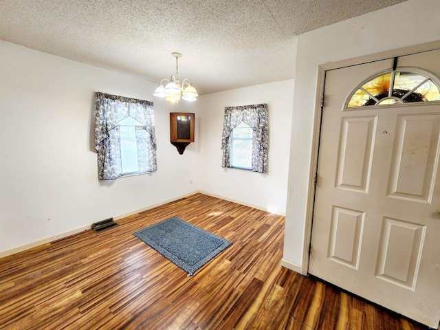 entryway with a textured ceiling, dark hardwood / wood-style floors, and an inviting chandelier