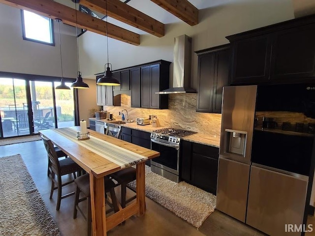 kitchen with wall chimney range hood, beamed ceiling, backsplash, decorative light fixtures, and stainless steel range with gas cooktop