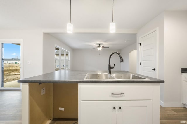 kitchen with hardwood / wood-style flooring, a kitchen island with sink, sink, white cabinets, and pendant lighting