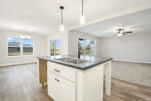 kitchen with a center island with sink, hardwood / wood-style flooring, hanging light fixtures, white cabinets, and a kitchen bar