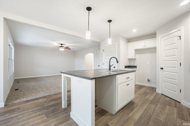 kitchen with sink, pendant lighting, dark wood-type flooring, white cabinets, and a kitchen island with sink