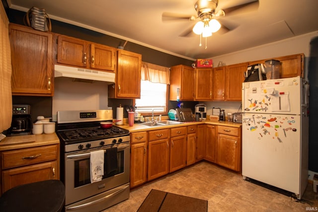 kitchen featuring ceiling fan, white refrigerator, crown molding, sink, and stainless steel gas range