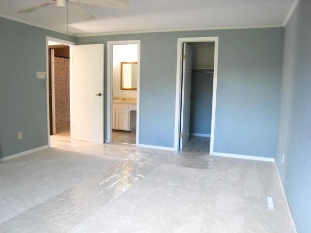 unfurnished bedroom featuring ceiling fan, a spacious closet, crown molding, ensuite bathroom, and a closet