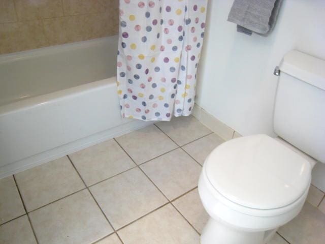 bathroom with tile patterned floors, toilet, and shower / bathtub combination with curtain