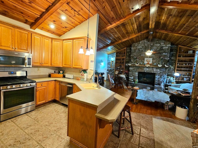 kitchen featuring a stone fireplace, kitchen peninsula, stainless steel appliances, a kitchen bar, and pendant lighting