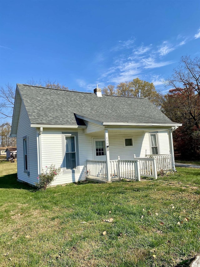 back of house with a chimney, a yard, and roof with shingles
