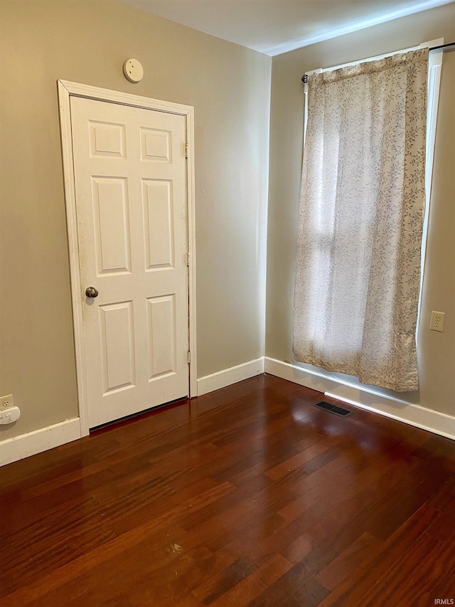 empty room featuring baseboards, visible vents, and dark wood-style floors