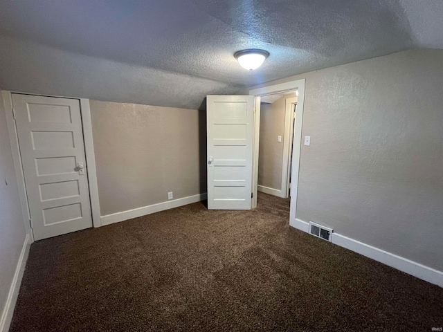 interior space with a textured ceiling, dark carpet, and vaulted ceiling