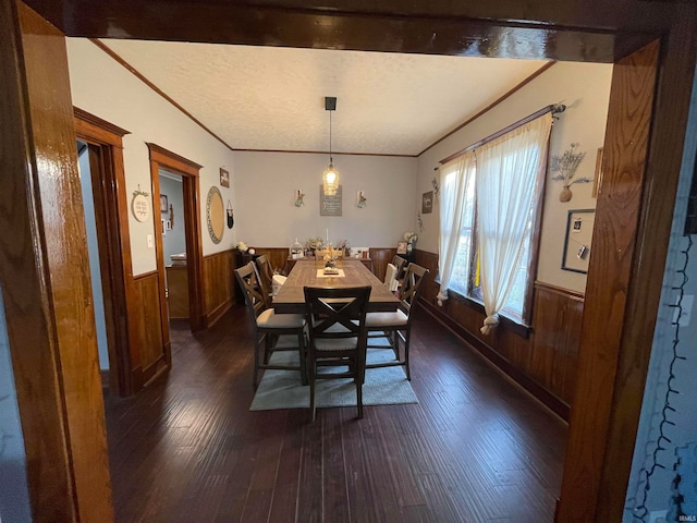 dining room with dark wood-type flooring, crown molding, a textured ceiling, and wooden walls