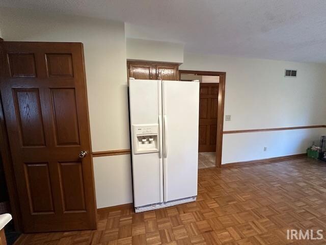 kitchen featuring a textured ceiling, white fridge with ice dispenser, and light parquet flooring