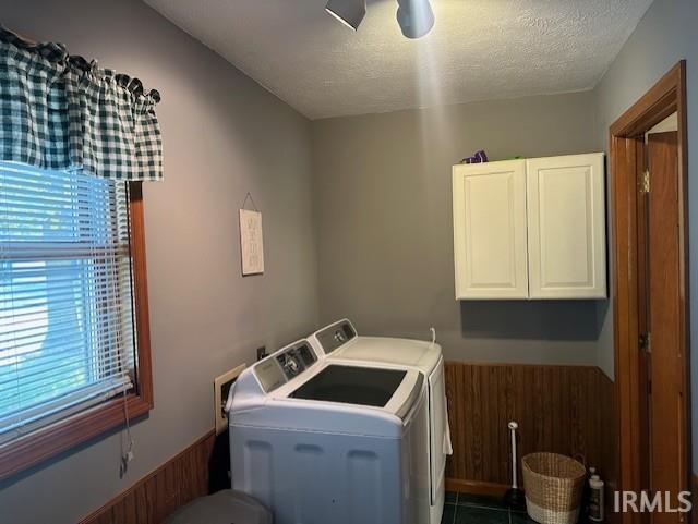 laundry room featuring wooden walls, washer and clothes dryer, cabinets, and a textured ceiling