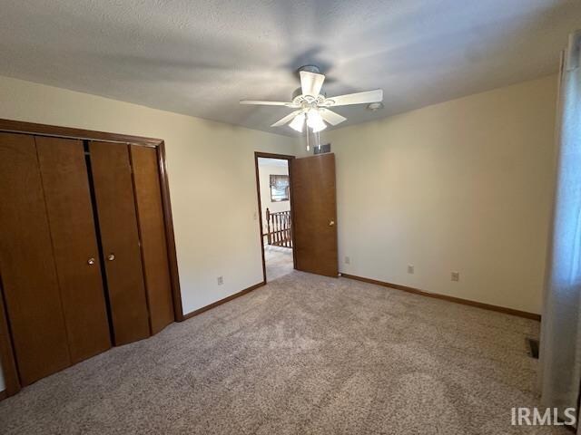 unfurnished bedroom with ceiling fan, light colored carpet, a closet, and a textured ceiling