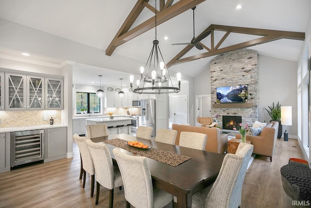 dining room featuring light wood-type flooring, a fireplace, bar area, wine cooler, and high vaulted ceiling