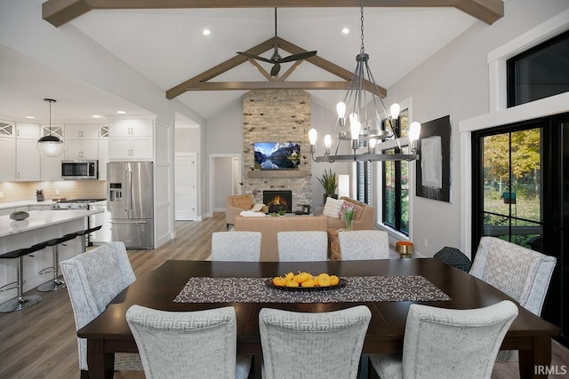 dining room featuring beamed ceiling, a chandelier, light wood-type flooring, and a fireplace