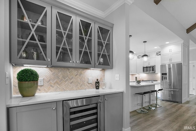 bar with tasteful backsplash, appliances with stainless steel finishes, pendant lighting, wine cooler, and hardwood / wood-style flooring