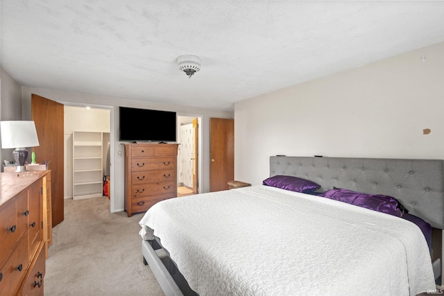 bedroom with light carpet, a closet, a textured ceiling, and a spacious closet