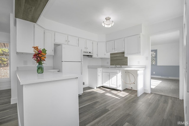 kitchen with kitchen peninsula, white cabinets, dark hardwood / wood-style floors, white fridge, and sink