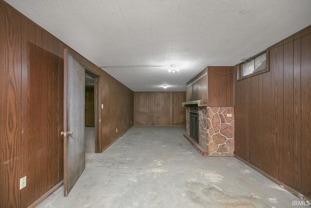 basement featuring a stone fireplace, a textured ceiling, and wooden walls