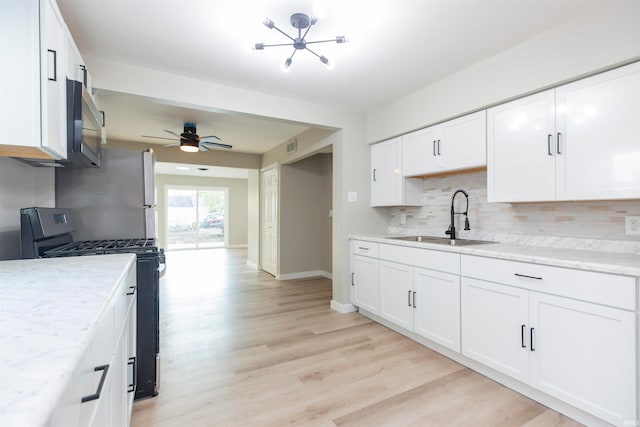 kitchen featuring sink, gas stove, white cabinetry, light hardwood / wood-style floors, and decorative backsplash