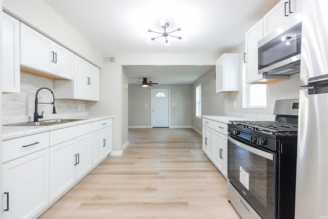 kitchen featuring appliances with stainless steel finishes, white cabinets, sink, and light wood-type flooring