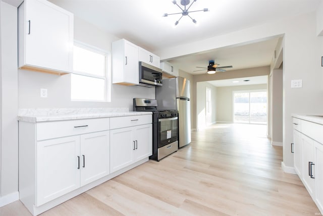 kitchen with light hardwood / wood-style flooring, stainless steel appliances, light stone countertops, white cabinets, and ceiling fan with notable chandelier