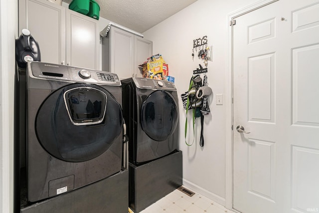 laundry area featuring washer and clothes dryer, cabinets, and a textured ceiling