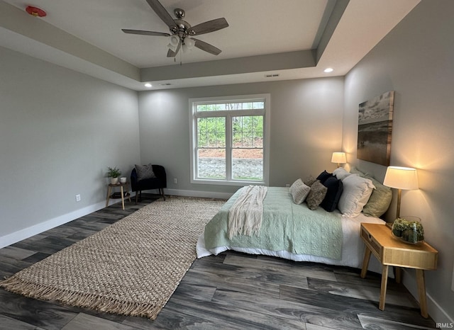 bedroom featuring dark hardwood / wood-style flooring, a tray ceiling, and ceiling fan