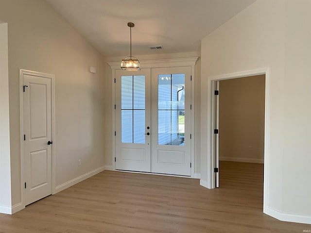 doorway with light hardwood / wood-style floors, an inviting chandelier, lofted ceiling, and french doors