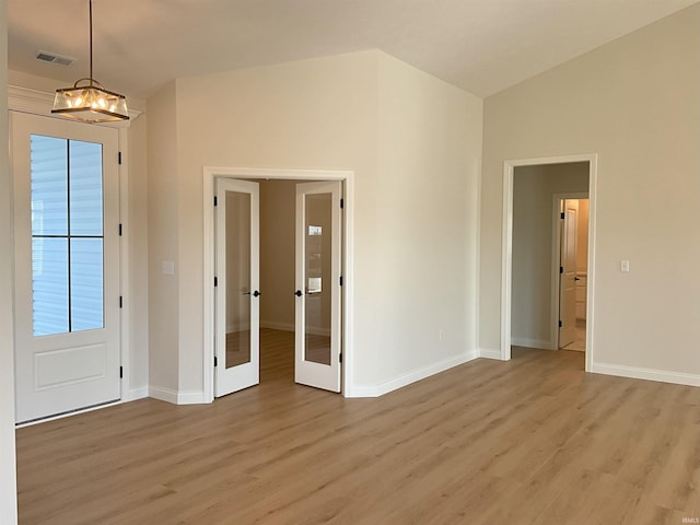 unfurnished room featuring french doors, light hardwood / wood-style floors, a chandelier, and vaulted ceiling