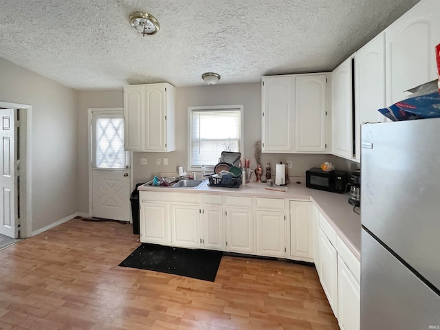 kitchen with white cabinetry, a textured ceiling, light wood-type flooring, and stainless steel refrigerator